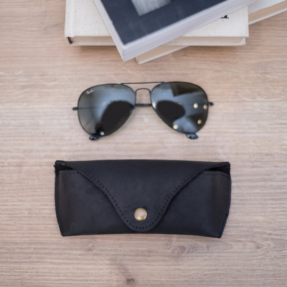 Lucent handcrafted black Crazy Horse leather sunglasses case with snap closure and aviator glasses on desk - Yubello