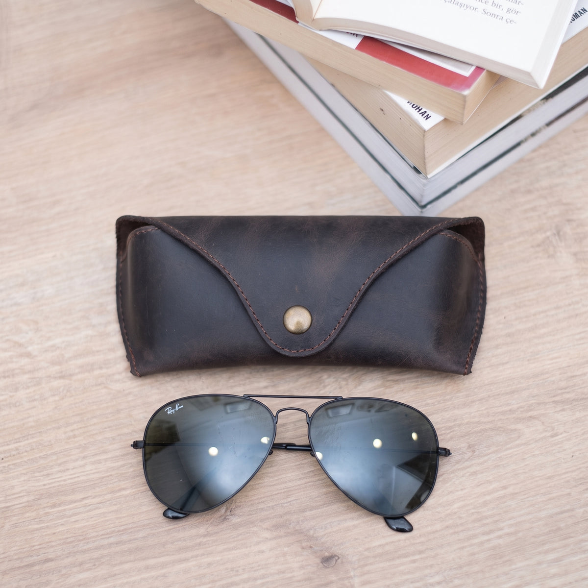 Lucent handcrafted dark brown Crazy Horse leather sunglasses case with snap closure and aviator glasses on desk - Yubello