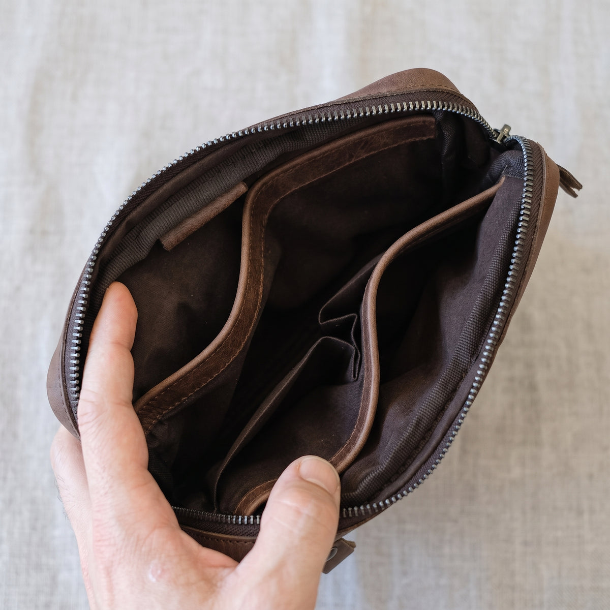 Nolen handcrafted brown Crazy Horse leather hand clutch bag held in hands with debossed logo - Yubello