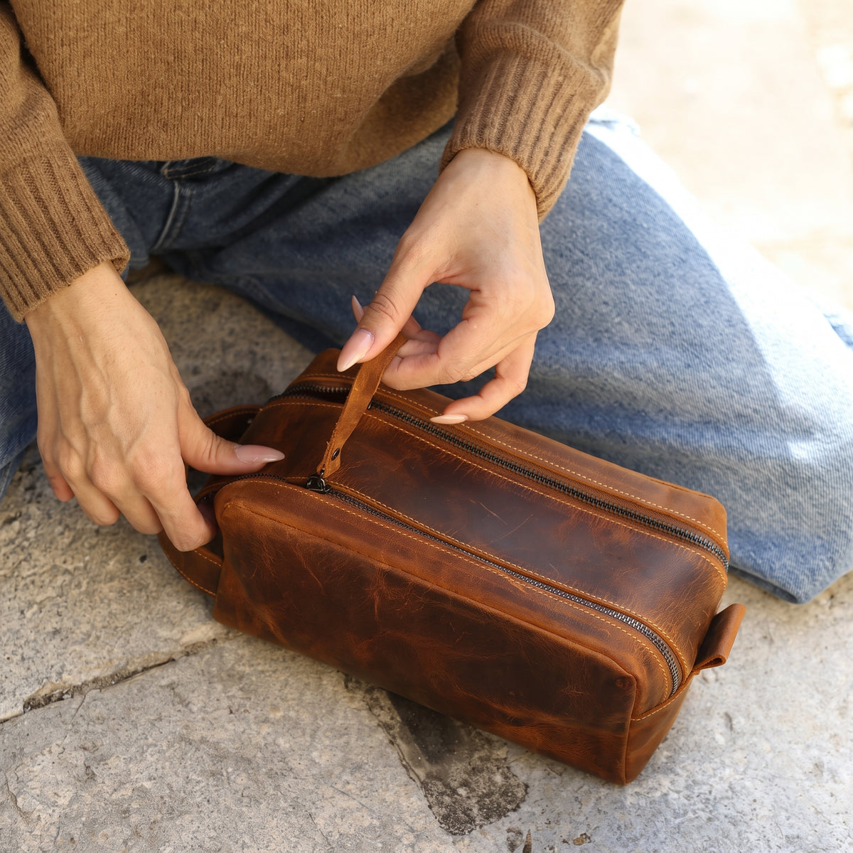 Thorne handcrafted dark brown leather double zip dopp kit travel bag held by side handle outdoors - Yubello